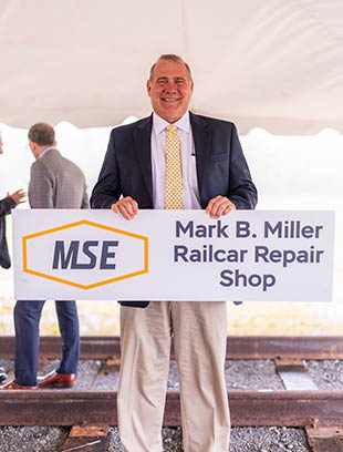 Mark B. Miller, former Vice President of Operations, holds the sign noting the new railcar repair complex will be named for him.